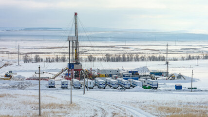 Expansive winter vista of industrial drilling rig complex amid snow-covered plain, featuring crew...