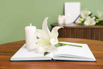 Beautiful lily flower, burning candle and book on wooden table in room