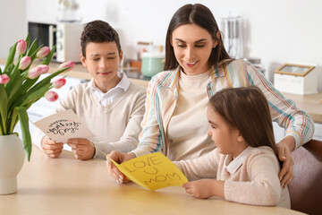 Young woman with greeting cards from her little children in kitchen. Mother's Day celebration