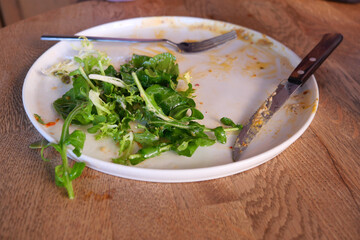 Leftover salad on a plate with utensils after meal