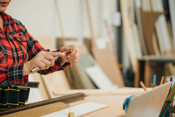 Woman in a red plaid shirt sharpening a pencil with a utility knife in a woodworking workshop. Ideal for carpentry, DIY projects, and banner displays with a focus on craftsmanship, Carpenter