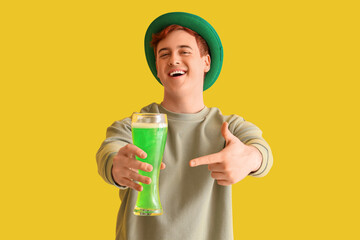 Young man pointing at beer on yellow background. St. Patrick's Day celebration