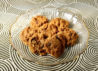 Yummy brown chocolate chip cookies biscuit sweet snacks on transparent plate isolated on horizontal table placemat surface background.