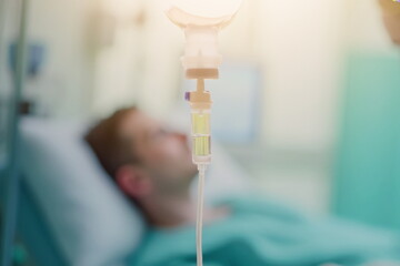 Close-up of IV drip with blurred surgical team operating in hospital. Medical treatment and healthcare concept.