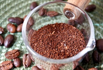 Close up grounded brown aromatic coffee organic dry drink ingredients in small transparent cup bowl...