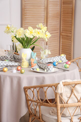 Festive Easter table setting with vase of flowers, cutlery, napkins and painted eggs