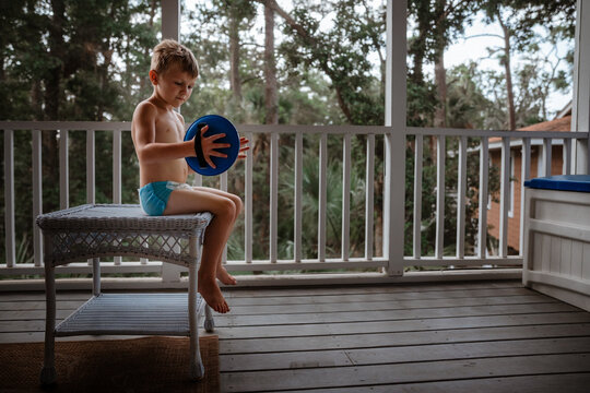 Toddler sitting on porch during summer playing with toy