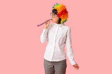 Funny young businesswoman with party blower on pink background. Fool's day