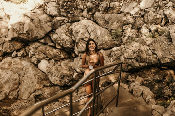 Attractive young woman in a bikini walking towards the rocky beach and enjoying her summer vacation