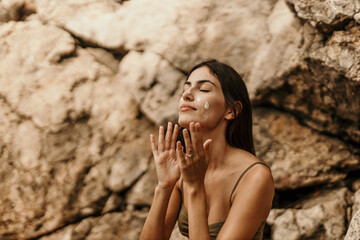 A young woman enjoying the beach while putting on sunscreen on her face.