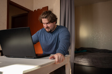Angry man working on laptop, stress and frustration during remote work, typing on a desk indoors.