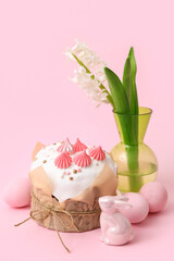 Delicious Easter cake, painted eggs, rabbit and hyacinth in vase on pink background