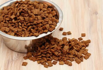 Detail of bowl with pet food inside. Food bowl and scattered granules around wooden table.