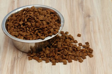 Detail of bowl with pet food inside. Food bowl and scattered granules around wooden table. Flat lay.