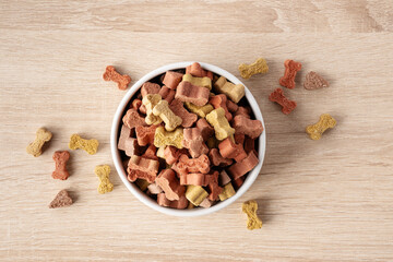 Dry dog food in a shape of bones in bowl on wooden floor background top view. Plate full of mineral healthy dog food. Pet snack in white bowl on floor.
