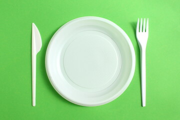 Disposable plastic white tableware lies on a green background.	