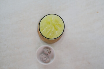 Top View Of Fresh Kedondong Juice With Ice Cubes In A Clear Glass On A Wooden Coaster, Accompanied...
