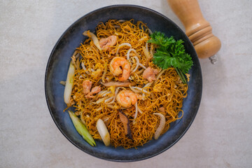 Appetizing Stir-Fried Noodles With Shrimp, Chicken, Vegetables, And Fresh Parsley Served In A Black Bowl On A Light Surface With A Pepper Grinder.