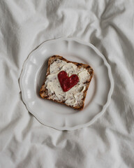 Valentine's Day breakfast - toast with butter and jam in the shape of a heart on a light background, top view