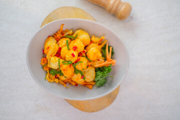 Crispy Fried Tofu With Spicy Chili And Salt Seasoning Garnished With Fresh Scallions And Parsley Served In A Bowl On A Wooden Board For A Tasty Snack.