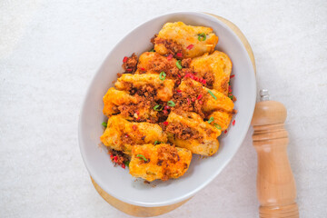 Golden Brown Eggplant With Savory Beef Floss Topping Served In A White Bowl, Enhanced With Fresh Herbs And Red Chili For A Flavorful And Spicy Bite.