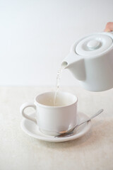 Pouring Hot Water Into White Ceramic Tea Cup With Saucer And Spoon On Light Surface In Minimalist Setting.