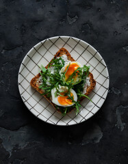 Sandwich with cream cheese, boiled egg, arugula on a dark background
