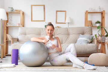 Sporty young woman with bottle of water and fitball at  home