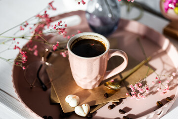 morning coffee in a pink ceramic cup on a background of flowers in a vase, gypsophila, white chocolate, coffee on a tray, breakfast in sunlight, food photo, still life with coffee and chocolate