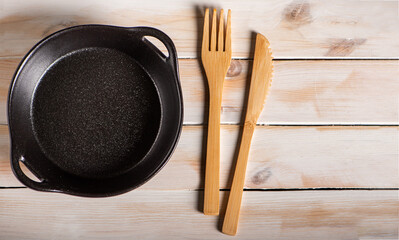 Empty black ceramic plate in a pan style next to wooden cutlery on a rustic white wooden table, top...