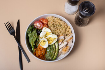 Bowl with eggs, vegetables, couscous and meat with black cutlery on beige background top view