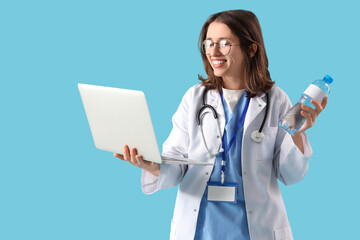 Female doctor with bottle of water and laptop on blue background