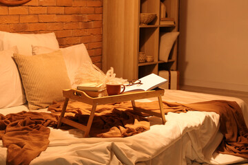 Tray with books, tea cup, eyeglasses and pampas grass in bedroom at night
