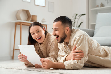 Happy young couple with refund form lying on floor at home