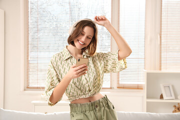 Beautiful young woman in headphones with mobile phone dancing at home