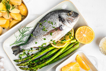 Fresh raw Dorado with asparagus spices, herbs, lemon and salt over white background.
