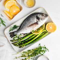 Fresh raw Dorado with asparagus spices, herbs, lemon and salt over white background.