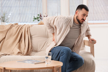 Young man suffering from back pain on sofa at home