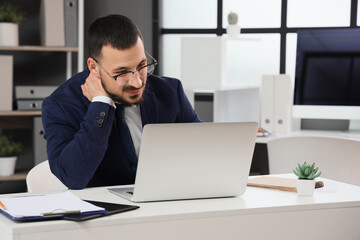 Young businessman suffering from neck pain at table in office