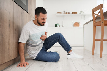 Young man suffering from chest pain on floor in kitchen