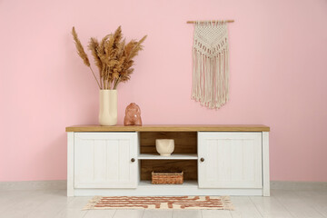 Vases with pampas grass on stand near pink wall in room