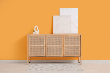 Stylish paintings with decor on commode near yellow wall in room