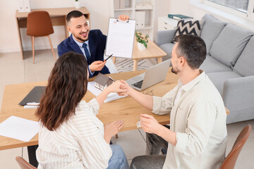 Male real estate agent with house rental agreement and couple at table in office