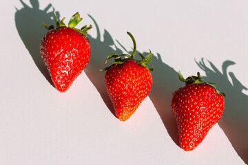 Ripped fresh delicious red strawberries lying diagonally in a row on the white table