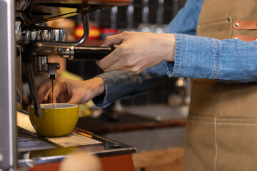 Close-up anonymous barista hands using professional coffee machine making hot espresso and pouring coffee to mug in cozy cafe, small businesses start up for young people lifestyle concept