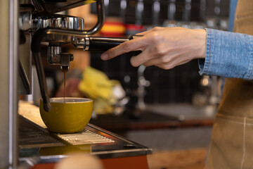 Close-up anonymous barista hands using professional coffee machine making hot espresso and pouring coffee to mug in cozy cafe, small businesses start up for young people lifestyle concept
