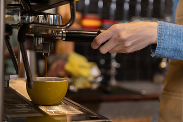 Close-up anonymous barista hands using professional coffee machine making hot espresso and pouring coffee to mug in cozy cafe, small businesses start up for young people lifestyle concept