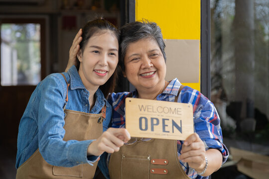 Asian 60s healthy senior barista worker female holding opening sign board pose in front of bakery shop retail small business owner start-up routine working, happy elderly retired pensioner lifestyle