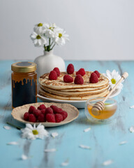 Large pancakes with fresh raspberries and honey or syrup for breakfast. Glass jar with golden honey. Natural sweetness, sugar free. Food concept, ready to eat. Snack, tasty dessert. Close up.