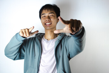 Asian teenager in white t-shirt and blue hoodie, posing happily pointing actively ahead